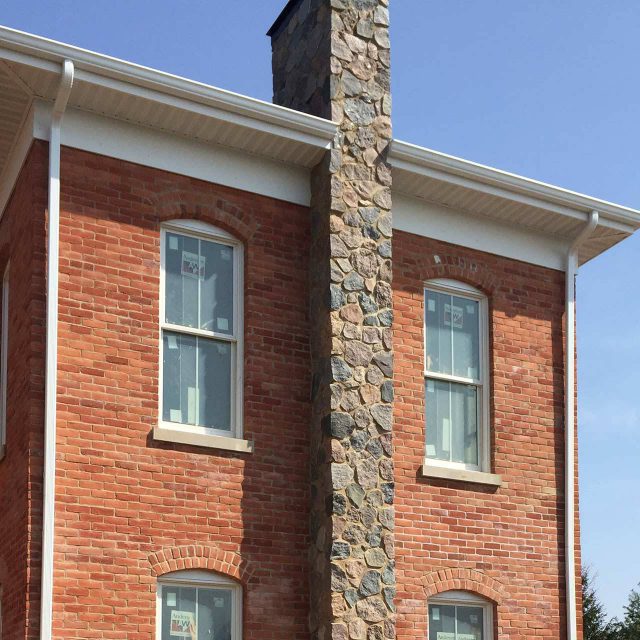 Exterior closeup of a red brick home with a large stone chimney and white gutters installed