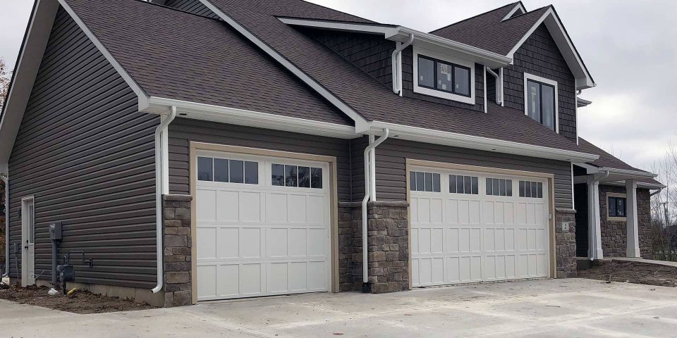 Newly built house with gray siding, white garage doors and a white gutter system
