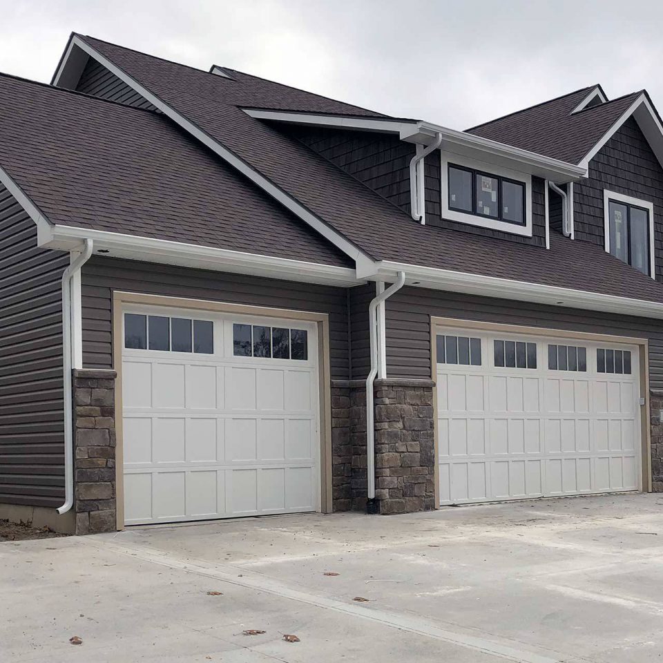 Newly built house with gray siding, white garage doors and a white gutter system