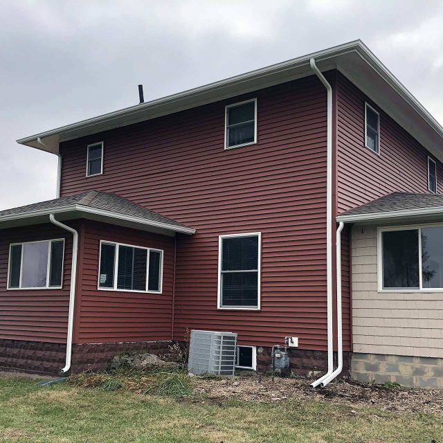 Exterior view of a house with red siding and a white gutter system