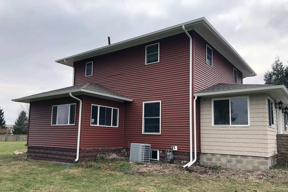 Exterior view of a house with red siding and a white gutter system