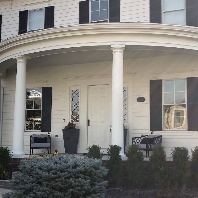 Front of a white house with black shutters and four columns